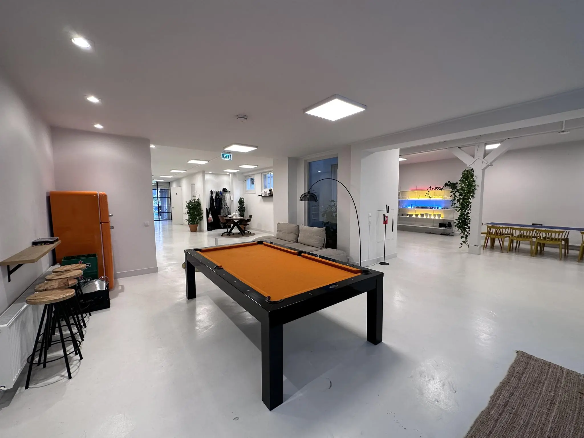 Modern kantoorinterieur aan de Bloemgracht met een oranje pooltafel, zithoek, eettafel en kleurrijke wandverlichting.