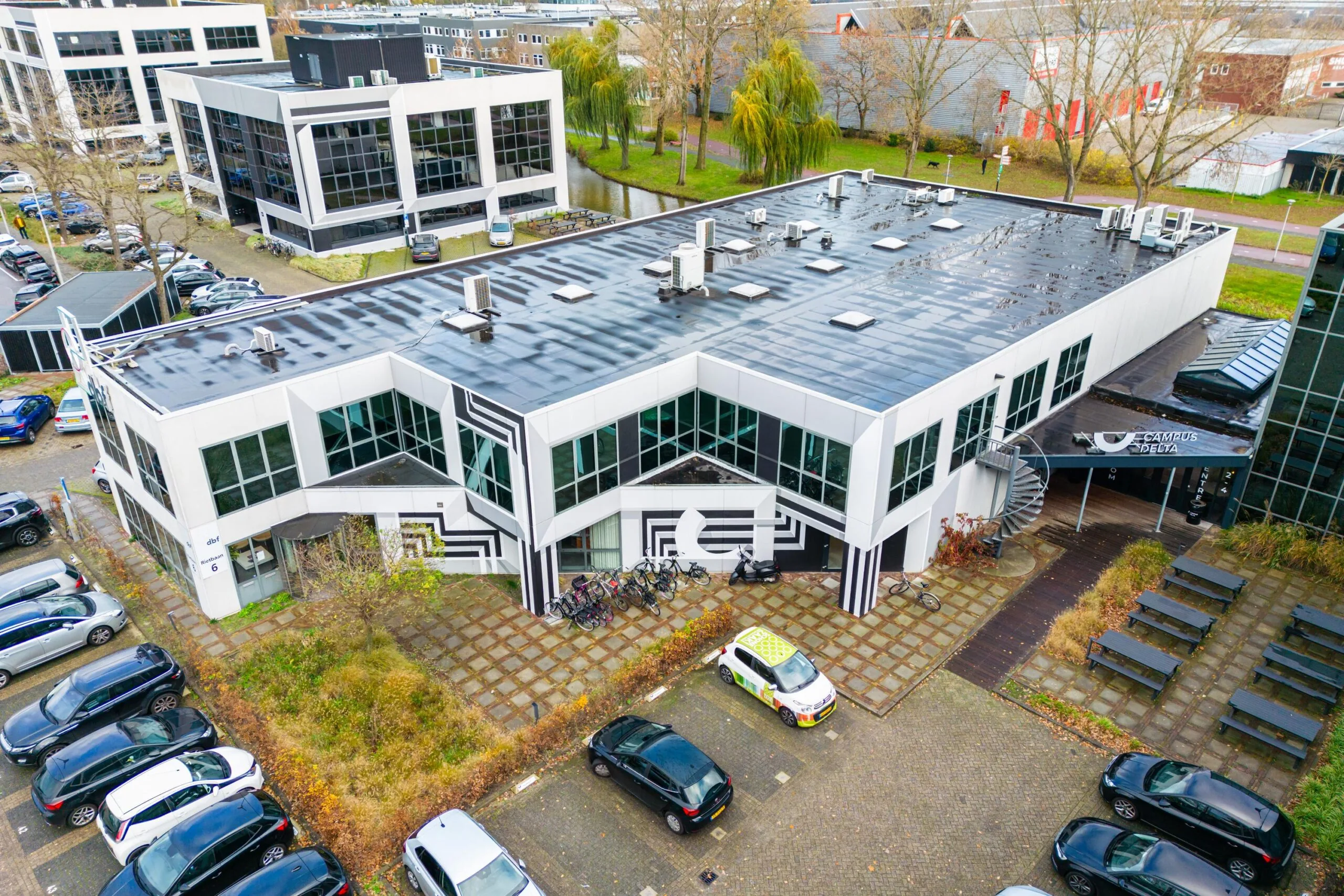 Aerial view of the modern white office building "Campus Delta" on Rietbaan, featuring geometric black-and-white wall patterns and surrounding parked cars.
