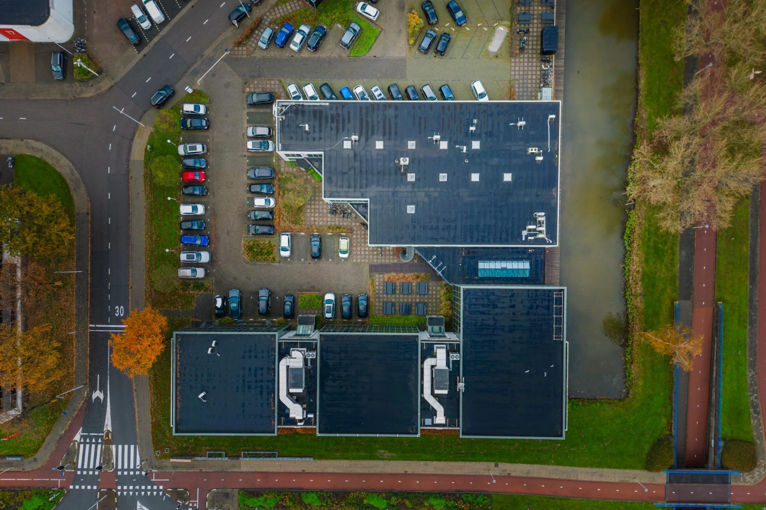 Aerial view of the Rietbaan building with adjacent parking lots, roads, and a canal in a suburban area.