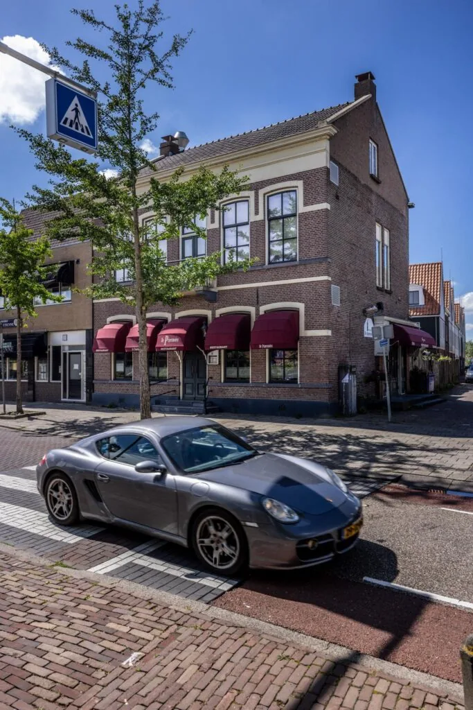 Grijze sportauto rijdt over een zebrapad voor restaurant 'De Pyramide' aan de Dorpsstraat.