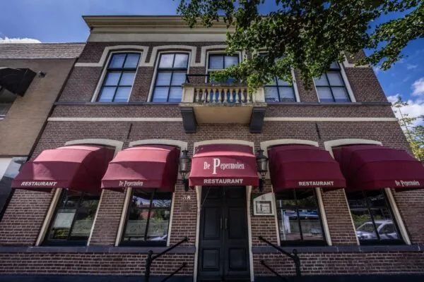 Voorgevel van restaurant De Pepermolen aan de Dorpsstraat met rode zonneschermen en klassieke bakstenen gevel.