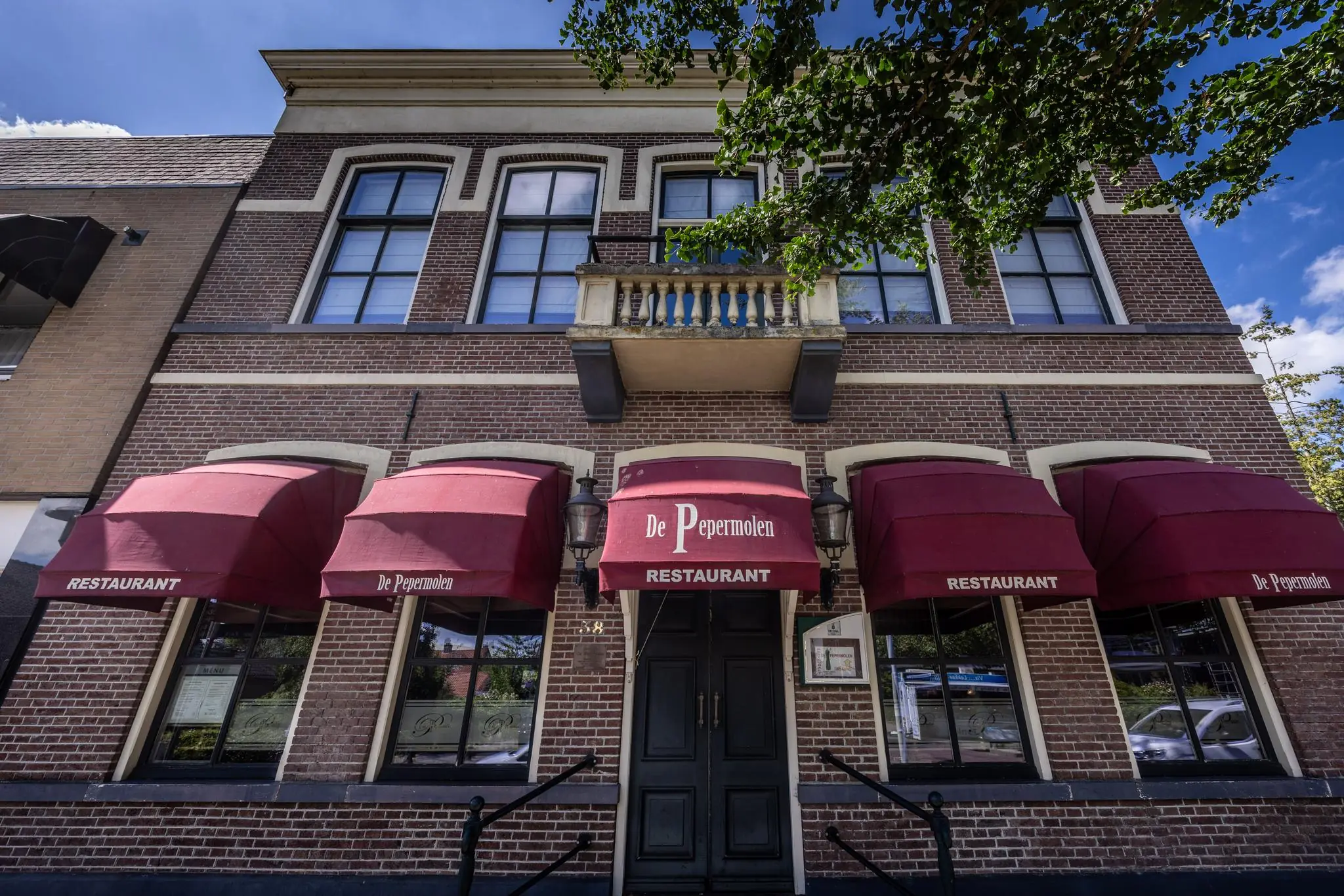 Voorgevel van restaurant De Pepermolen aan de Dorpsstraat met rode zonneschermen en klassieke bakstenen gevel.
