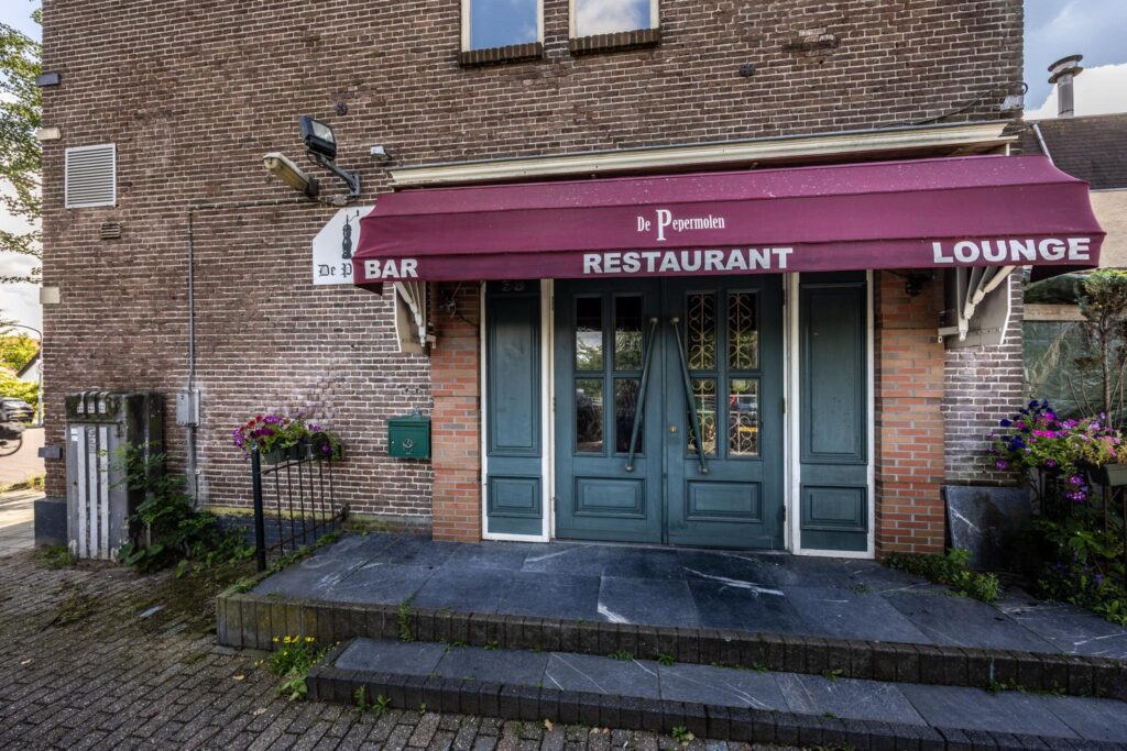Vooraanzicht van restaurant De Pepermolen met bordeauxrode zonwering en groene dubbele deur aan de Dorpsstraat.