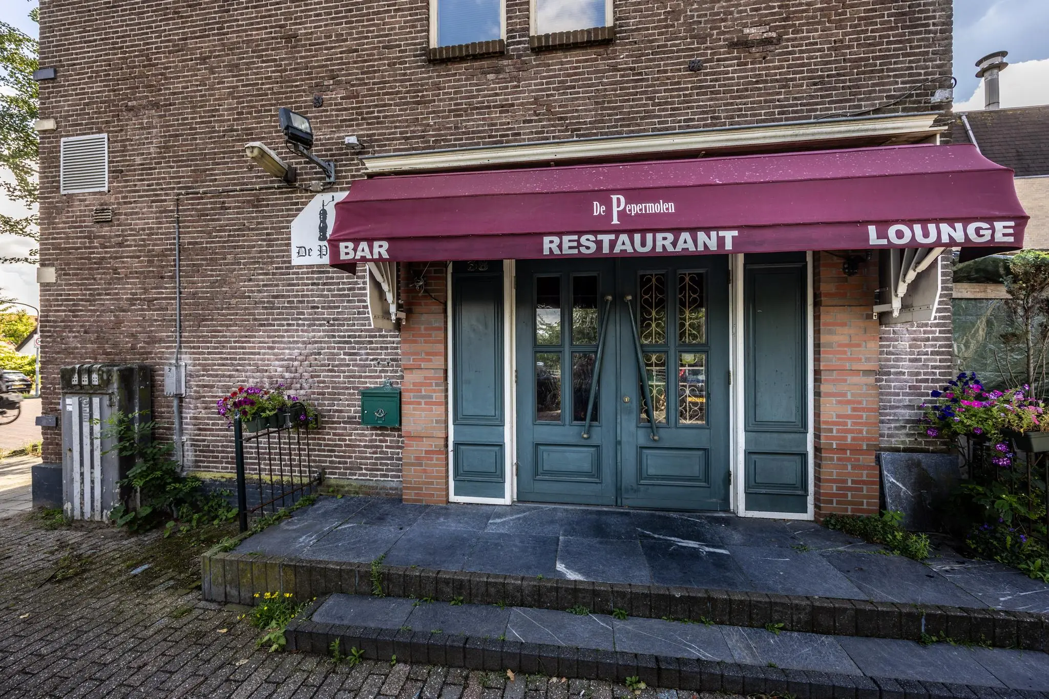 Vooraanzicht van restaurant De Pepermolen met bordeauxrode zonwering en groene dubbele deur aan de Dorpsstraat.