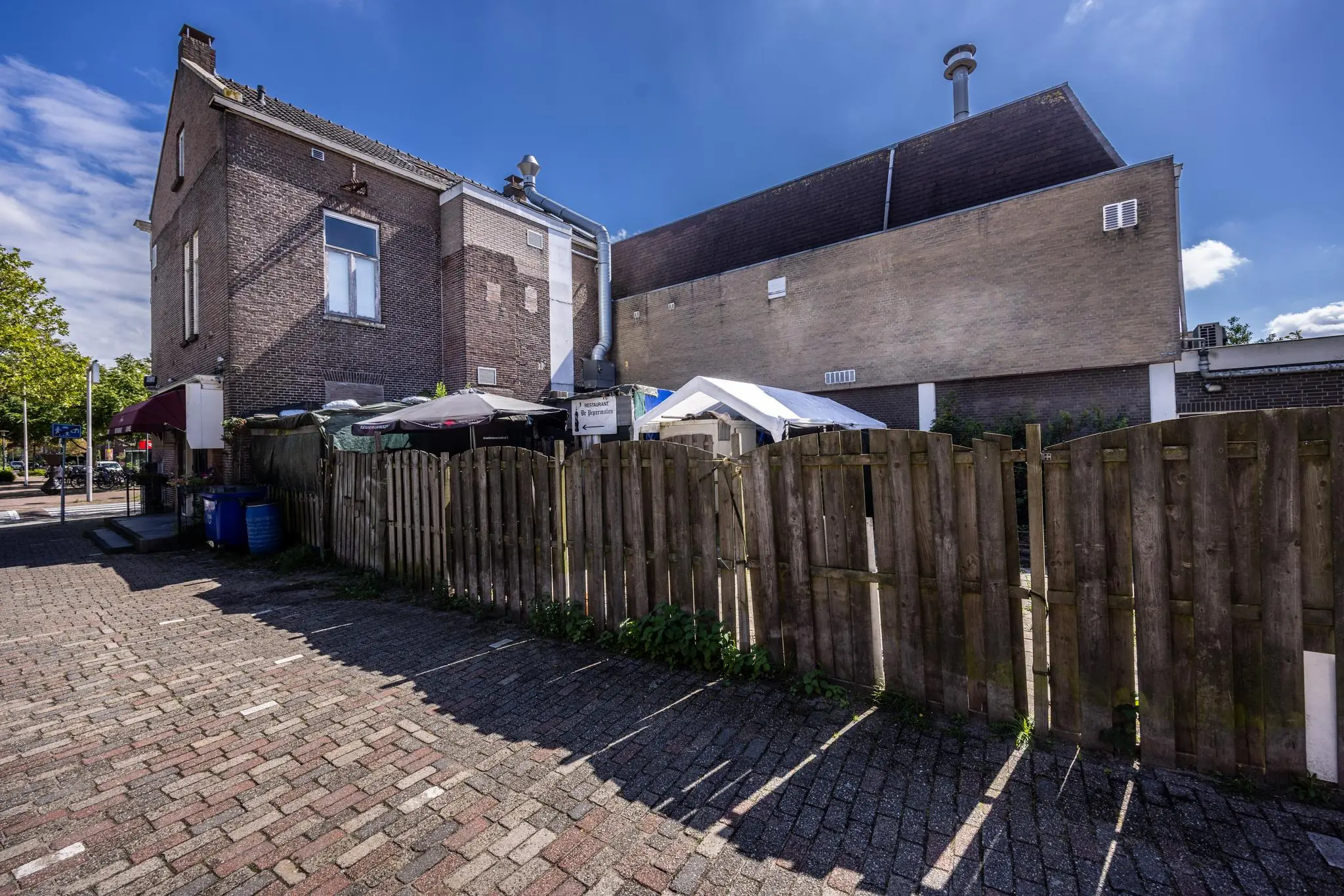 Achterkant van een gebouw aan de Dorpsstraat met houten schutting, parasols en ventilatiekanalen.