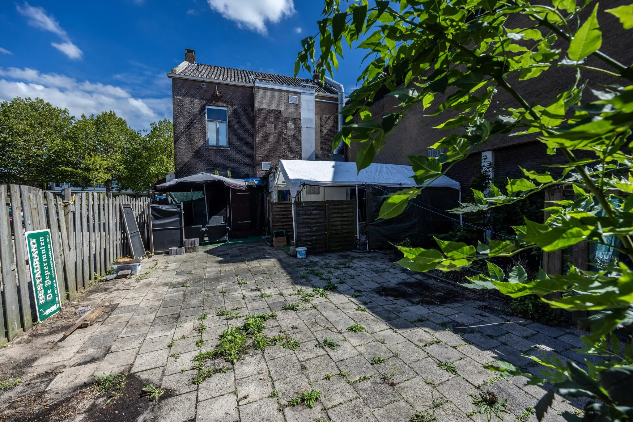 Achterzijde van een woning aan de Dorpsstraat met betegelde tuin, overkapping en verweerde omheining.