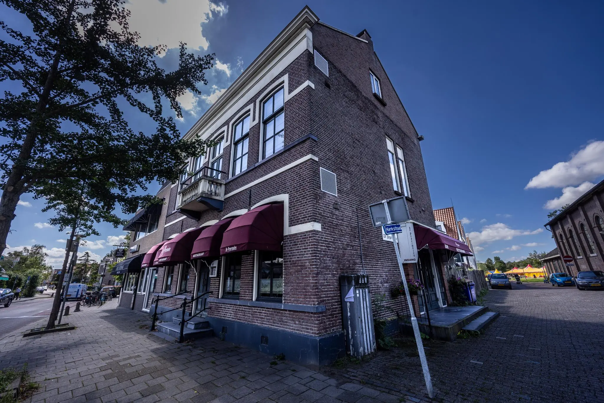 Hoekpand aan de Dorpsstraat met rode zonneschermen en straatnaambordje naar de Kerkstraat.