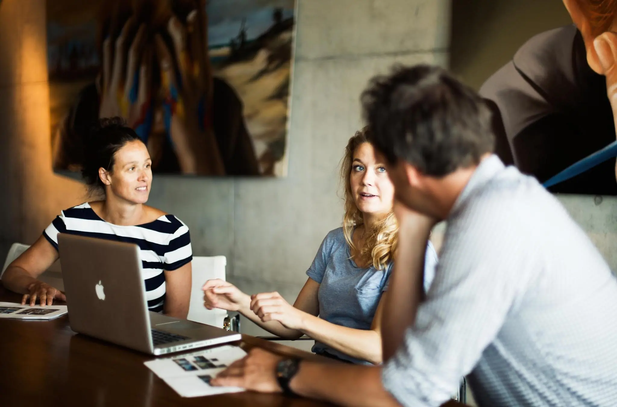 Drie mensen in gesprek tijdens een meeting met een laptop en documenten op tafel in een modern kantoor aan de Orteliuslaan.