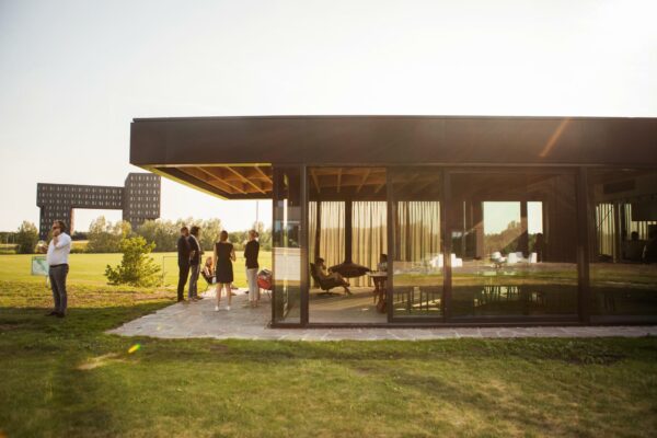 Moderne glazen kantoorpaviljoen aan de Orteliuslaan met groepje mensen buiten op het terras bij zonnig weer.