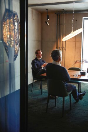 Twee mannen zitten aan een vergadertafel in een modern kantoor aan de Orteliuslaan, met warme verlichting en een kunstwerk aan de muur.