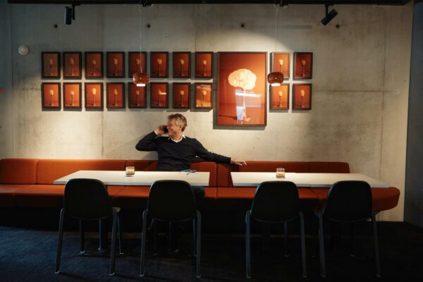 Man zit telefonerend aan een tafel in een moderne ruimte aan de Orteliuslaan, met kunstwerken van lepels en een bloemkool aan de muur.