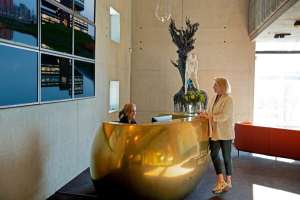 Vrouw bij de receptie van Creative Valley aan de Orteliuslaan, met gouden balie, kunstwerk en moderne inrichting.