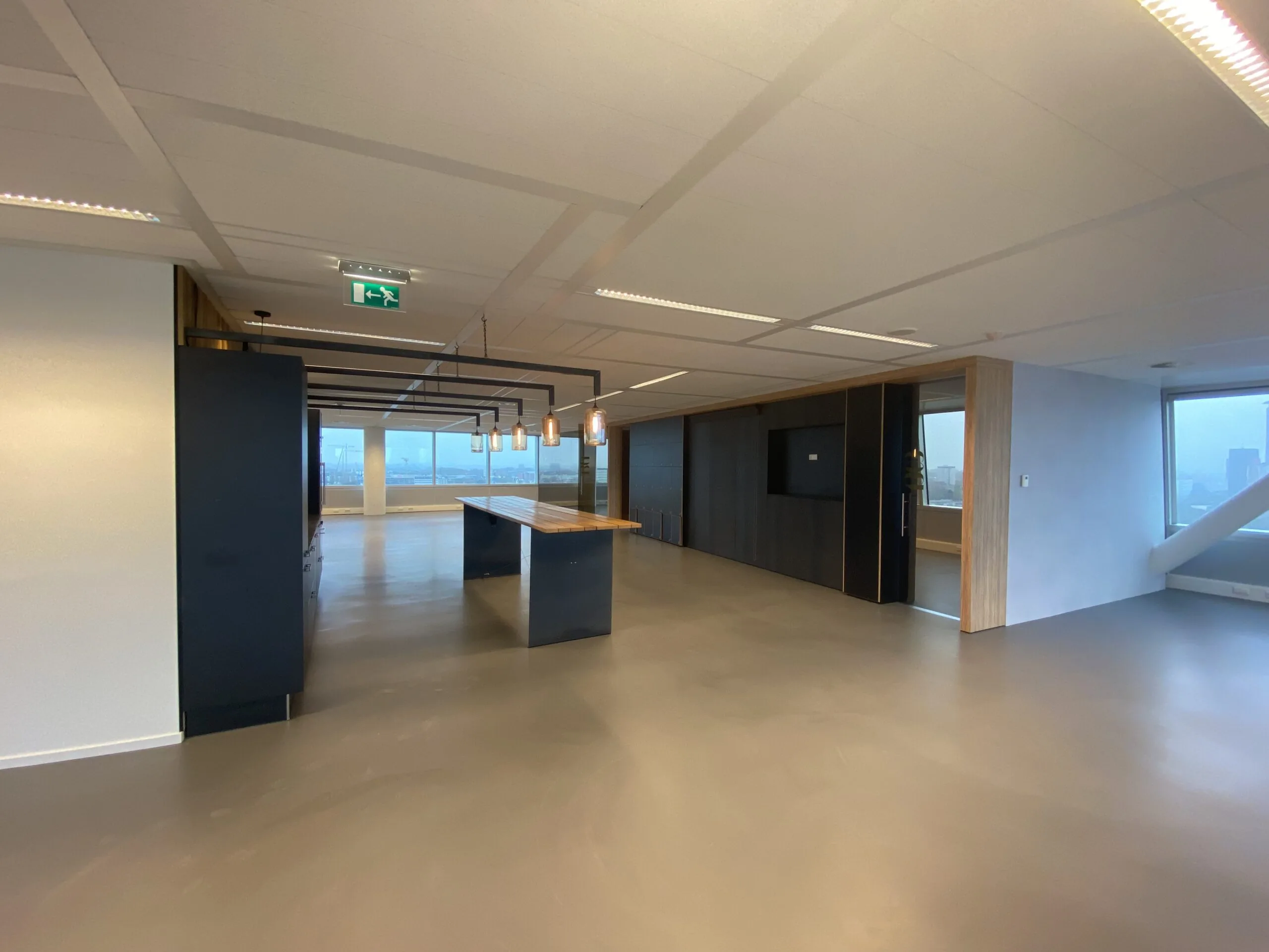 Moderne, open kantoorruimte met een lange houten tafel, hanglampen en grote ramen met uitzicht op de stad.