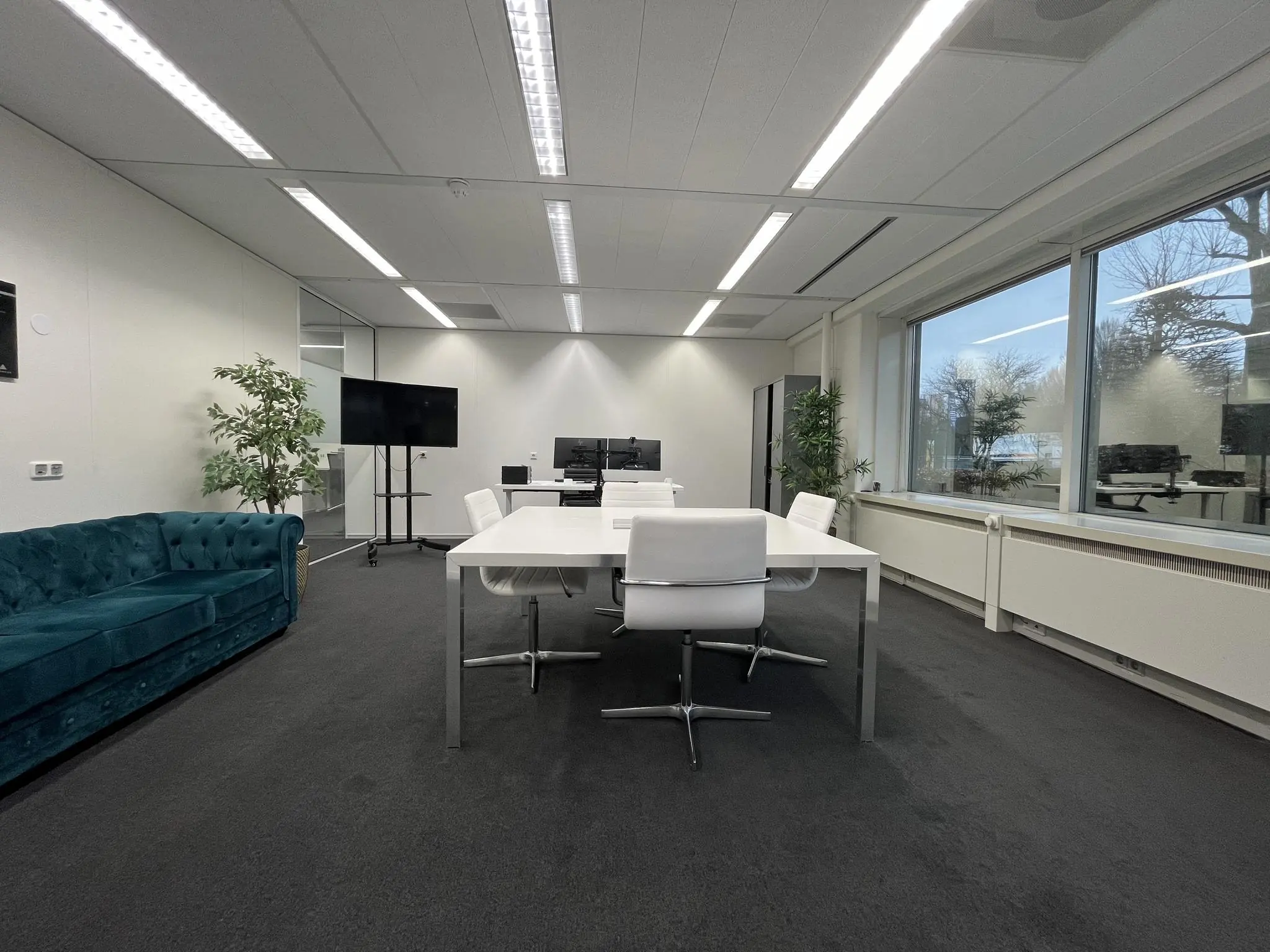 Moderne vergaderruimte aan de Savannahweg met witte tafels, bureaustoelen, een groene bank en grote ramen met uitzicht naar buiten.