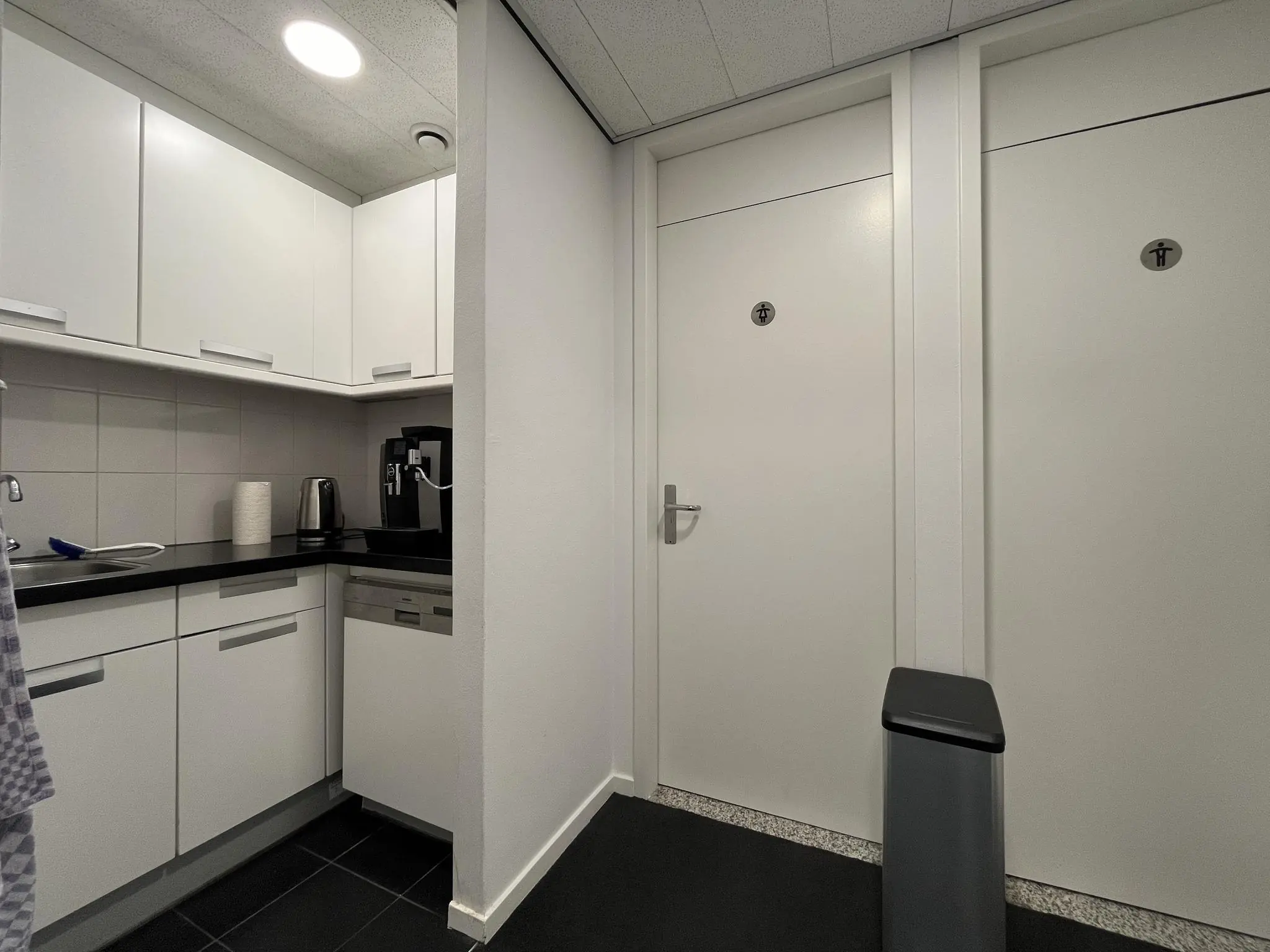 Kleine bedrijfskeuken met koffiezetapparaat en waterkoker naast twee toiletten met gescheiden voorzieningen.