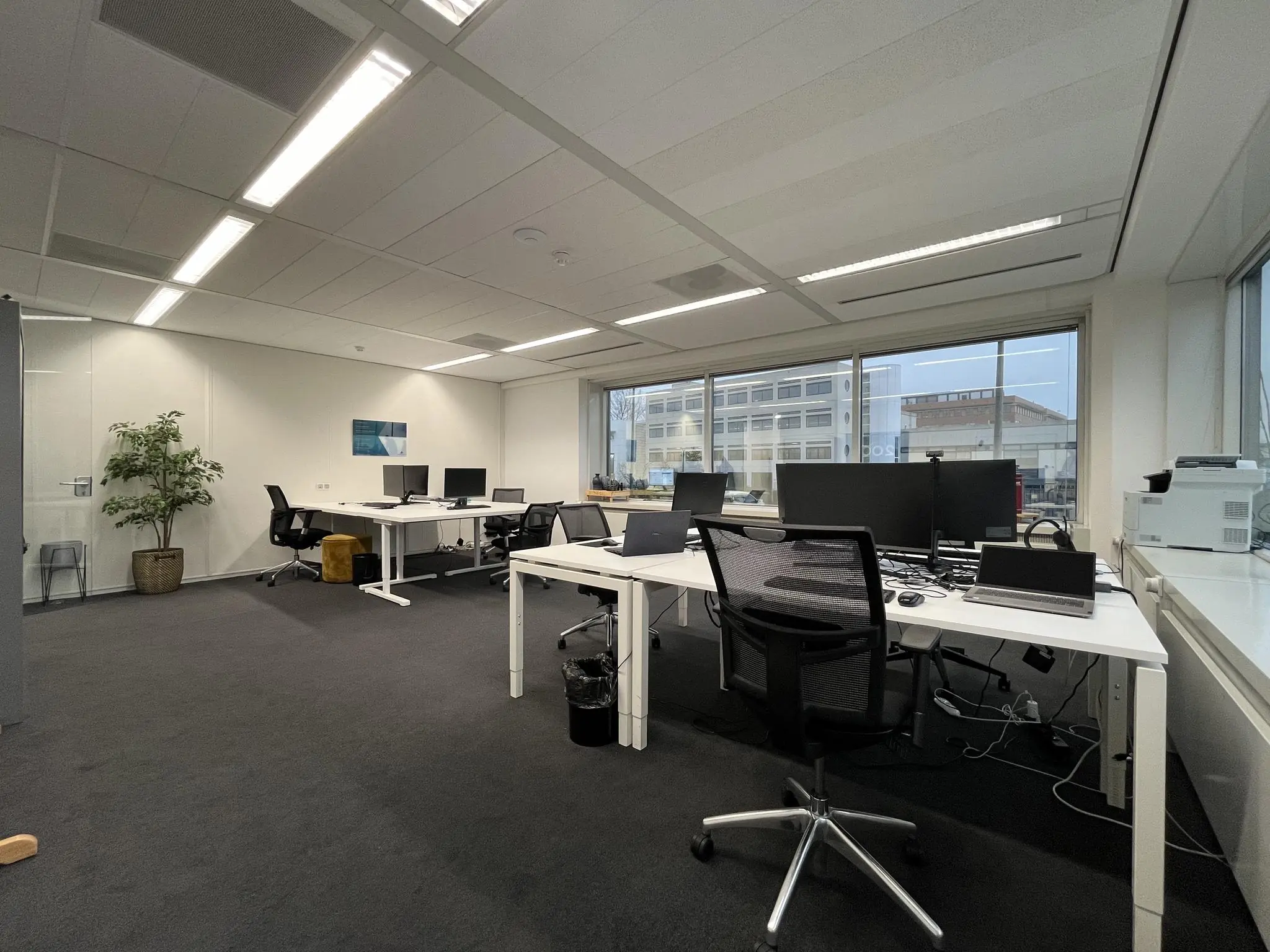 Moderne kantoorruimte aan de Savannahweg met meerdere bureaus, computerschermen en grote ramen met uitzicht op een industrieel gebouw.