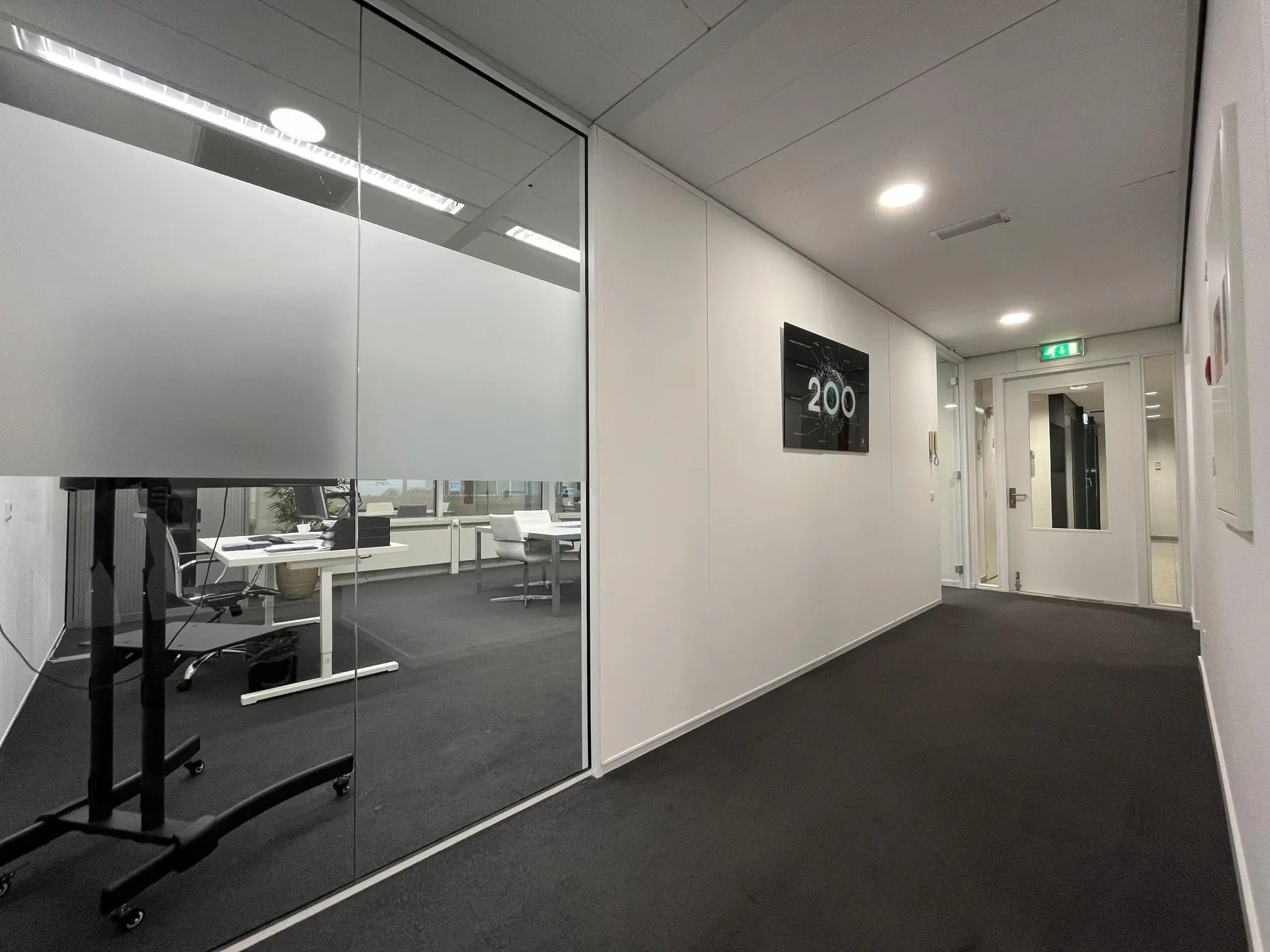 Moderne kantoorhal met glazen vergaderruimte en het kamernummer 200 aan de muur.