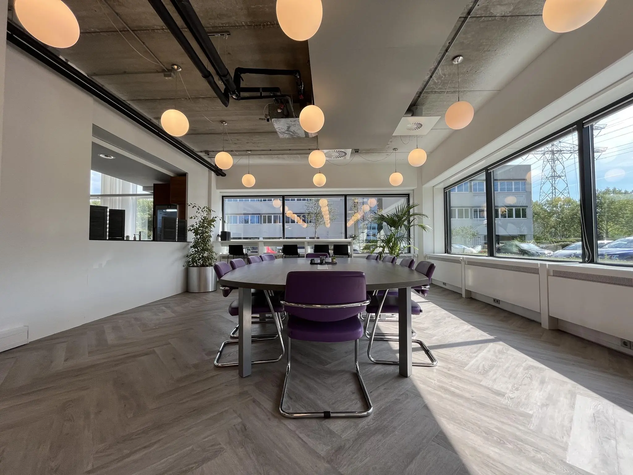 Moderne vergaderruimte aan de Savannahweg met paarse stoelen, een ovale tafel en grote ramen die veel daglicht binnenlaten.