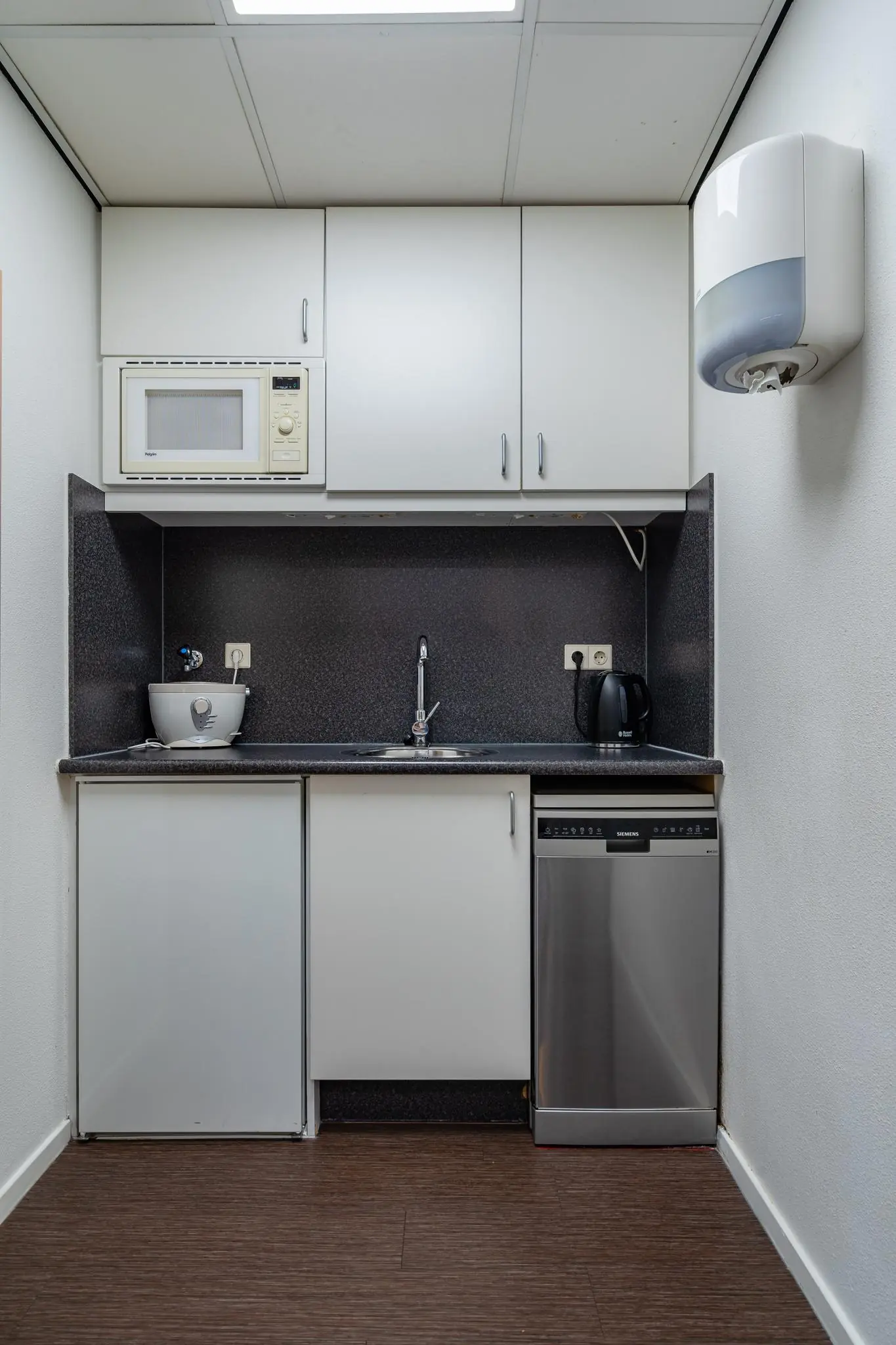 Kleine kitchenette aan de Barbizonlaan met magnetron, gootsteen, waterkoker en vaatwasser.
