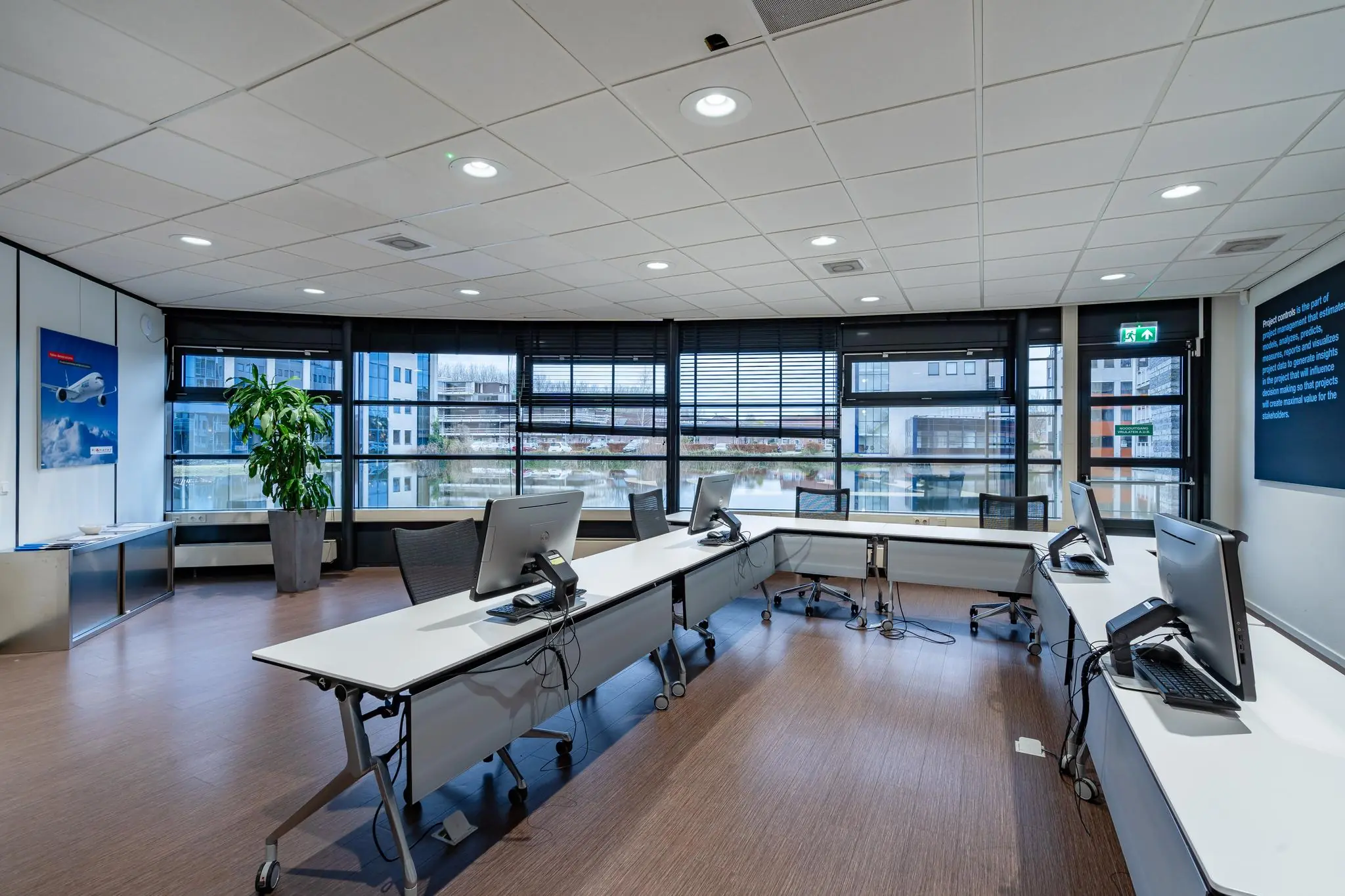 Modern ingerichte kantoorruimte aan de Barbizonlaan met gebogen bureaus, computers en uitzicht op een vijver en omliggende kantoorgebouwen.