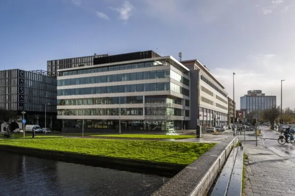 Straatbeeld van de Wibautstraat in Amsterdam met moderne kantoorgebouwen, waaronder Hotel Casa, en een groenstrook langs het water op de voorgrond.