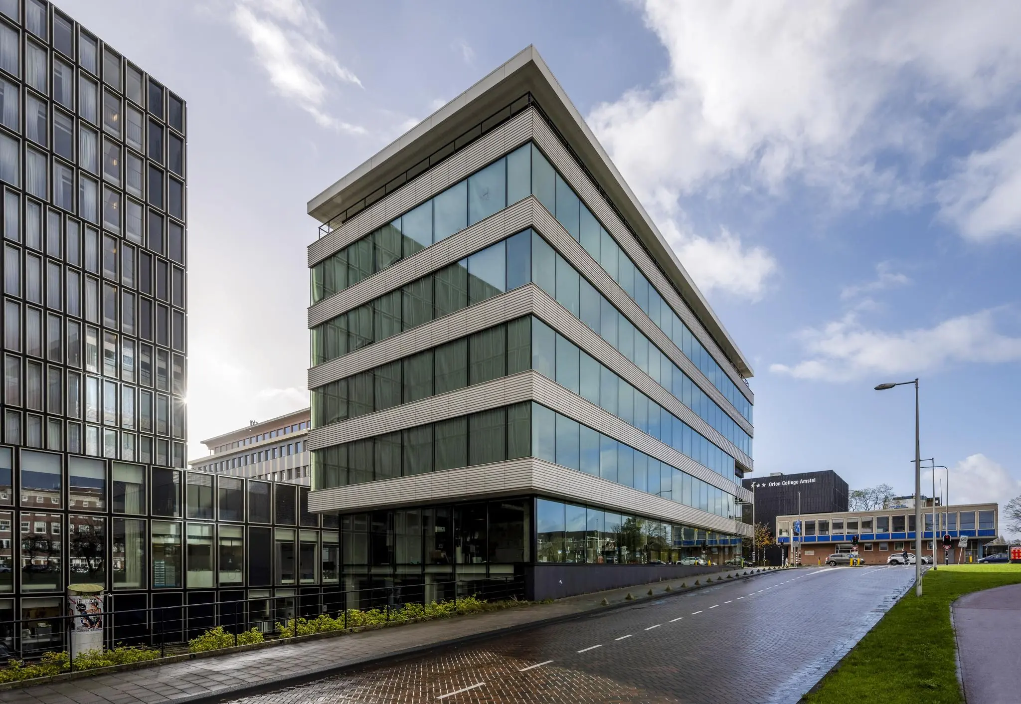Modern kantoorgebouw aan de Wibautstraat in Amsterdam met glazen gevels en een natgeregende weg.