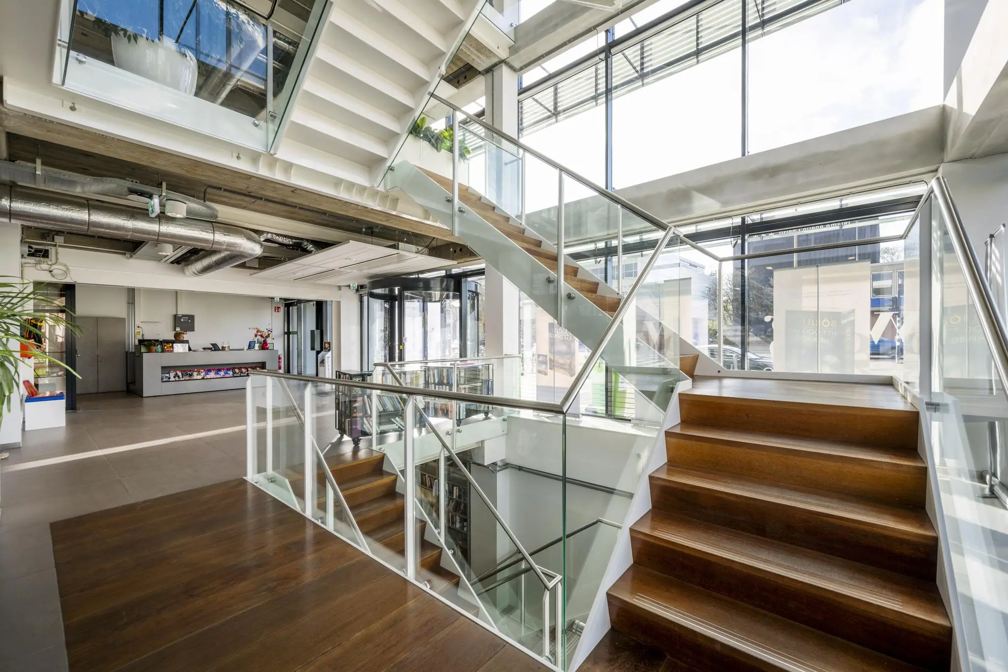 Moderne, lichte entreehal in een kantoorpand aan de Wibautstraat met een houten trap en glazen balustrades.