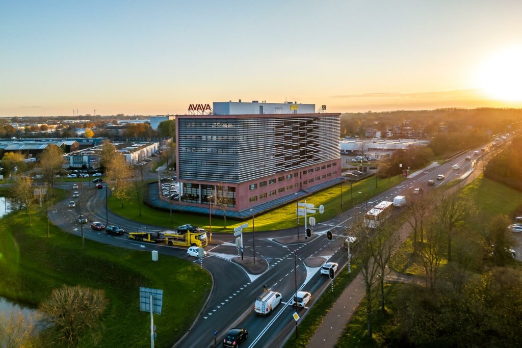 Luchtfoto van het Avaya-kantoorgebouw aan de Marconibaan in Nieuwegein bij zonsondergang met omliggende wegen en verkeer.