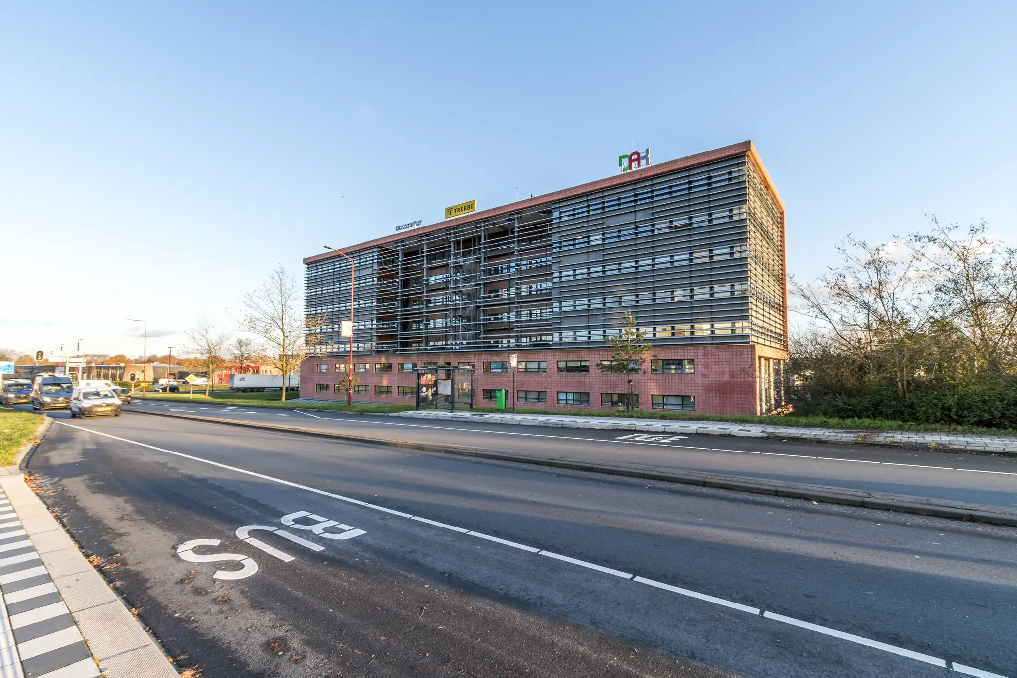 Kantoorgebouw aan de Marconibaan met bushalte op de voorgrond en verkeer op de weg.