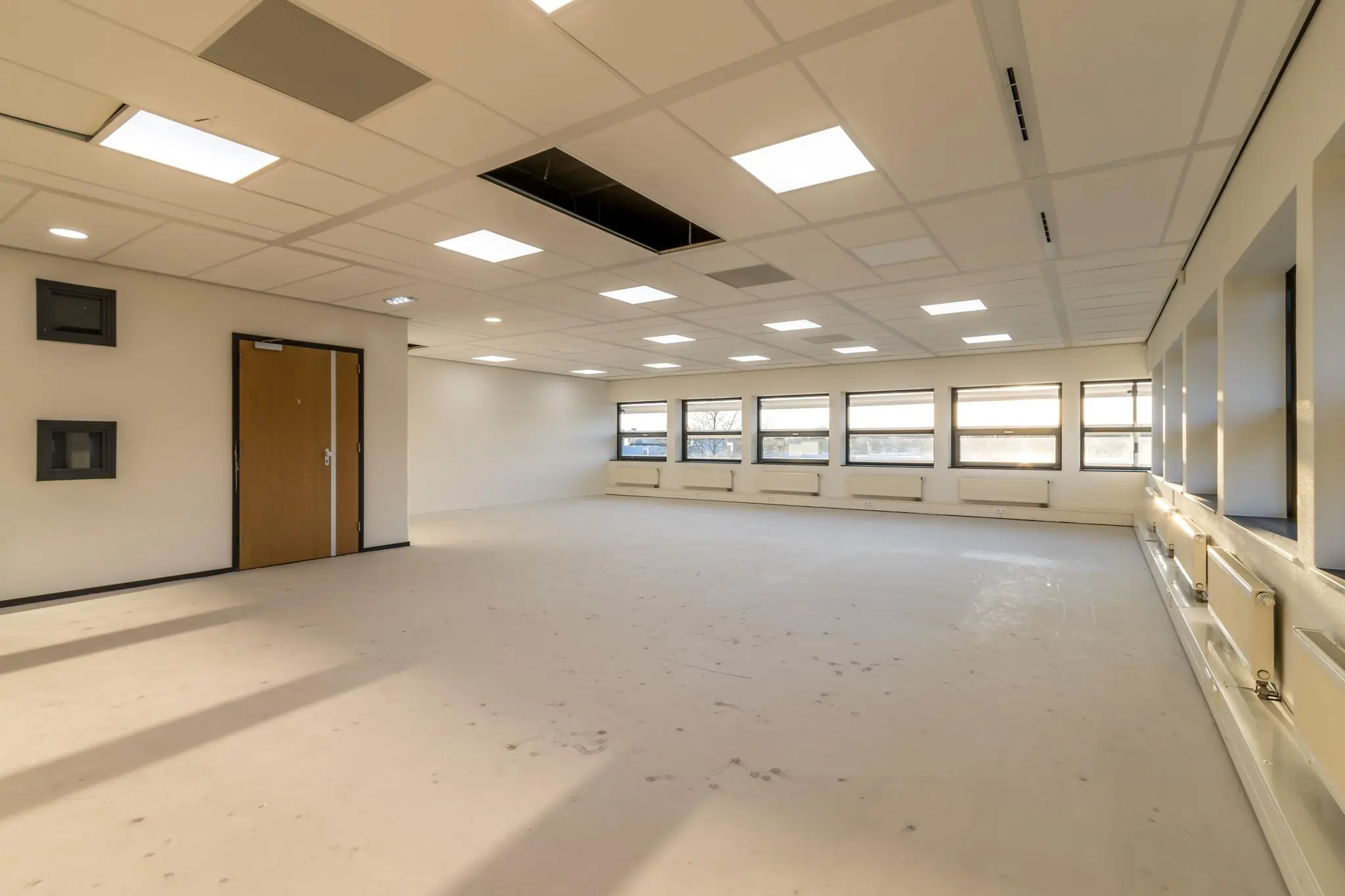 Leeg kantoorruimte aan de Marconibaan met systeemplafond, ramen en TL-verlichting.