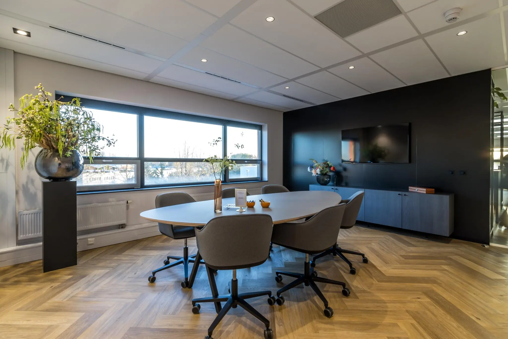 Moderne vergaderruimte aan de Marconibaan met ovale tafel, zes stoelen, houten visgraatvloer en grote ramen met uitzicht.