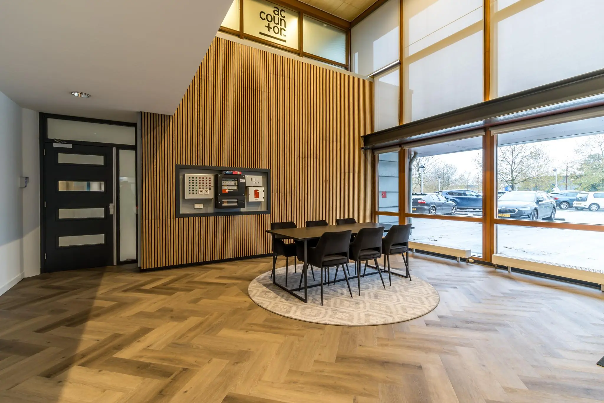 Moderne ontvangstruimte aan de Marconibaan met houten wandpanelen, een vergadertafel en grote ramen met uitzicht op de parkeerplaats.
