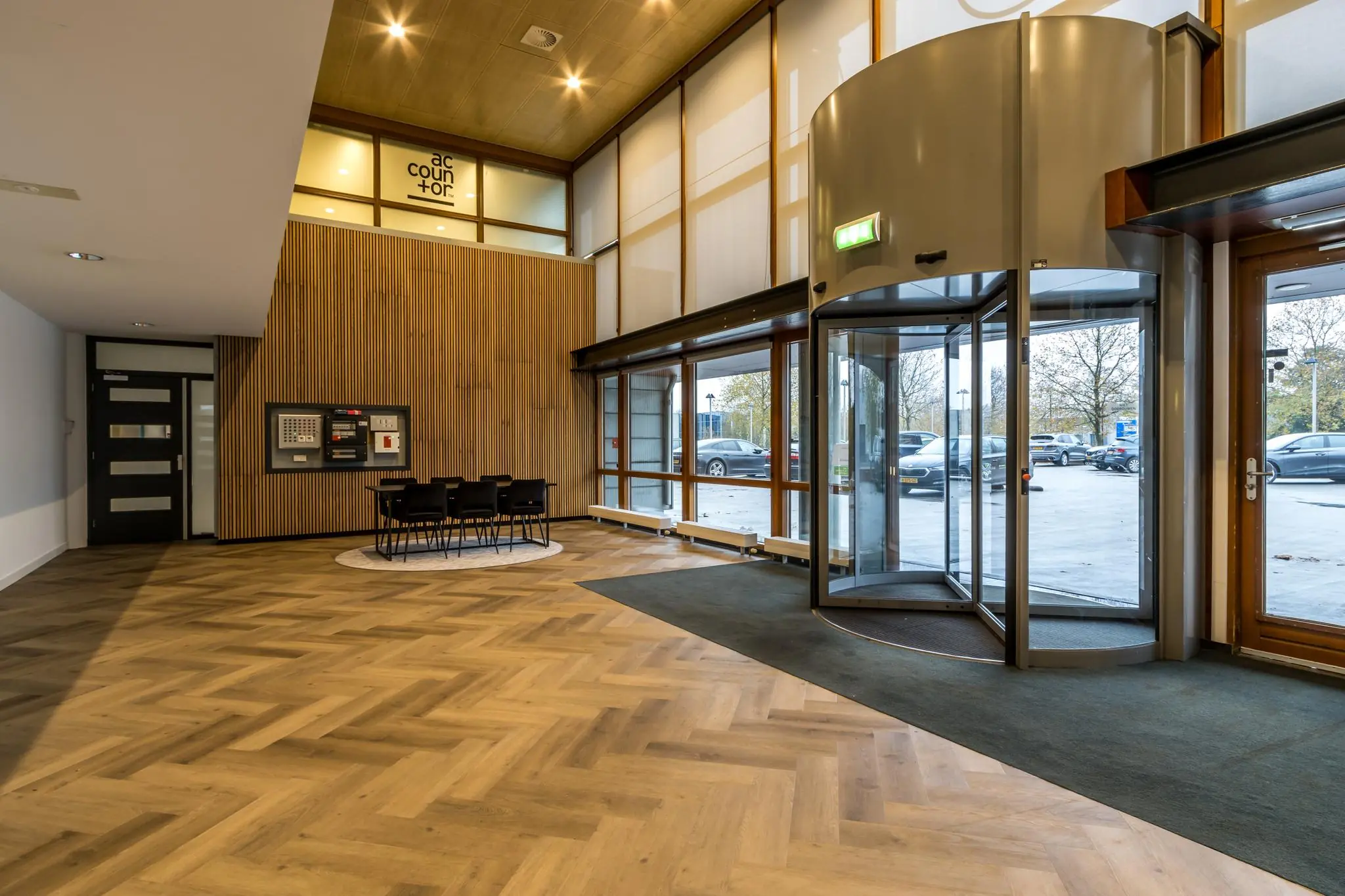 Ingang van een modern kantoorgebouw aan de Marconibaan met draaideur, houten vloer en wachtruimte met stoelen.