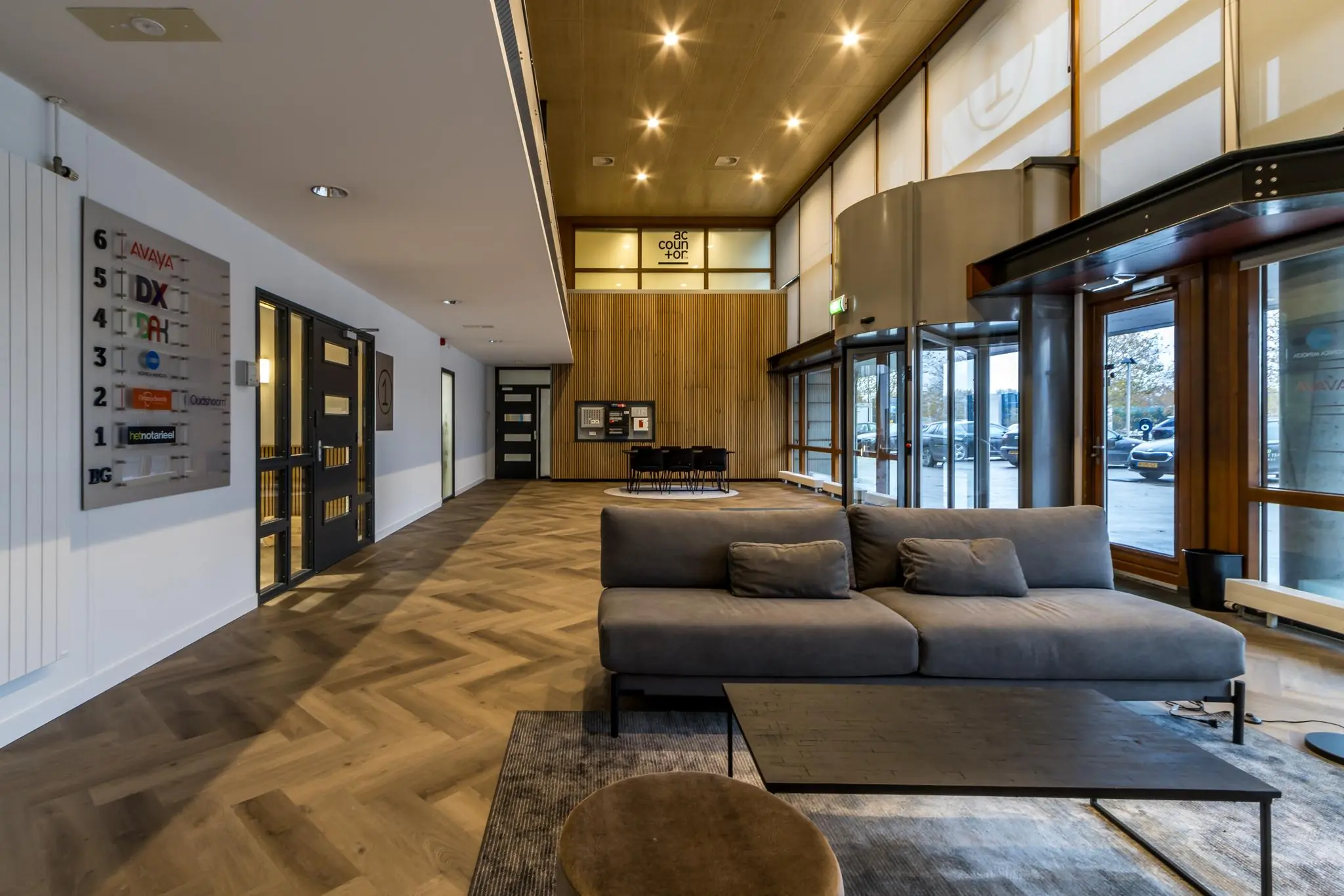Moderne entreehal van een kantoorpand aan de Marconibaan met houten vloer, zithoek en glazen draaideur.