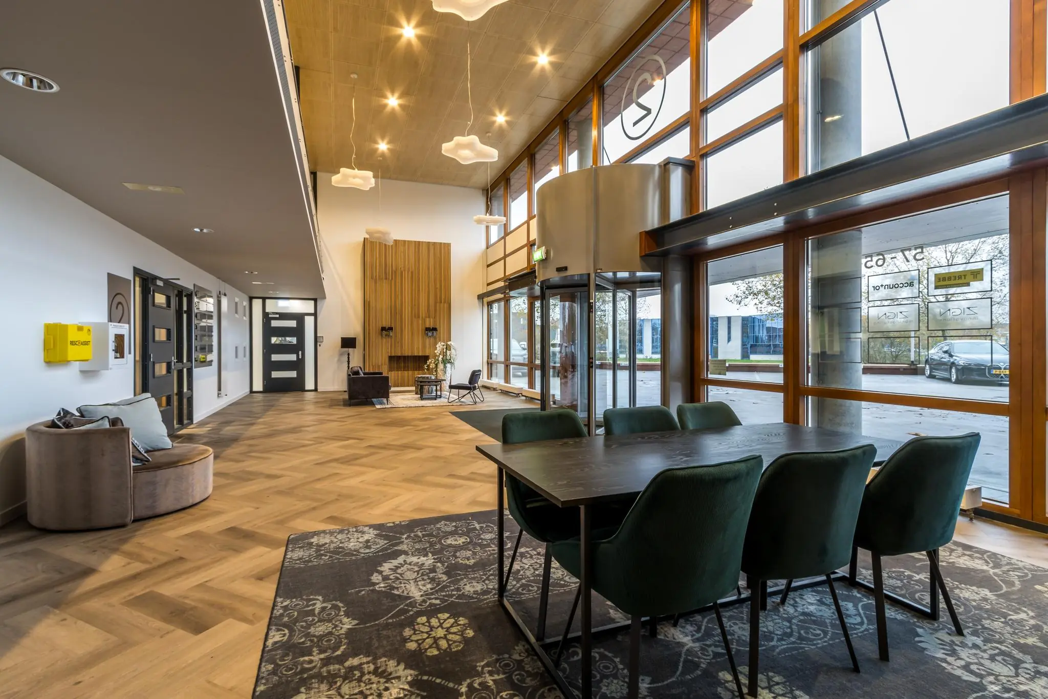 Moderne ontvangstruimte aan de Marconibaan met houten vloer, grote ramen en een zitgedeelte met groene stoelen.