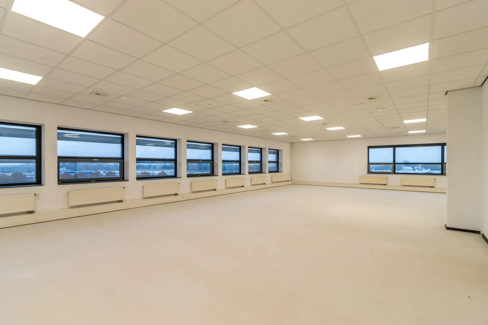 Leeg kantoorruimte met systeemplafond en grote ramen aan de Marconibaan.