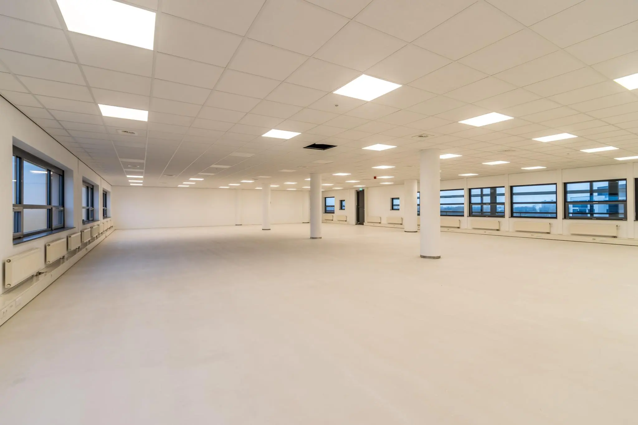 Ruime, lege kantoorruimte aan de Marconibaan met witte muren, systeemplafond en grote ramen.