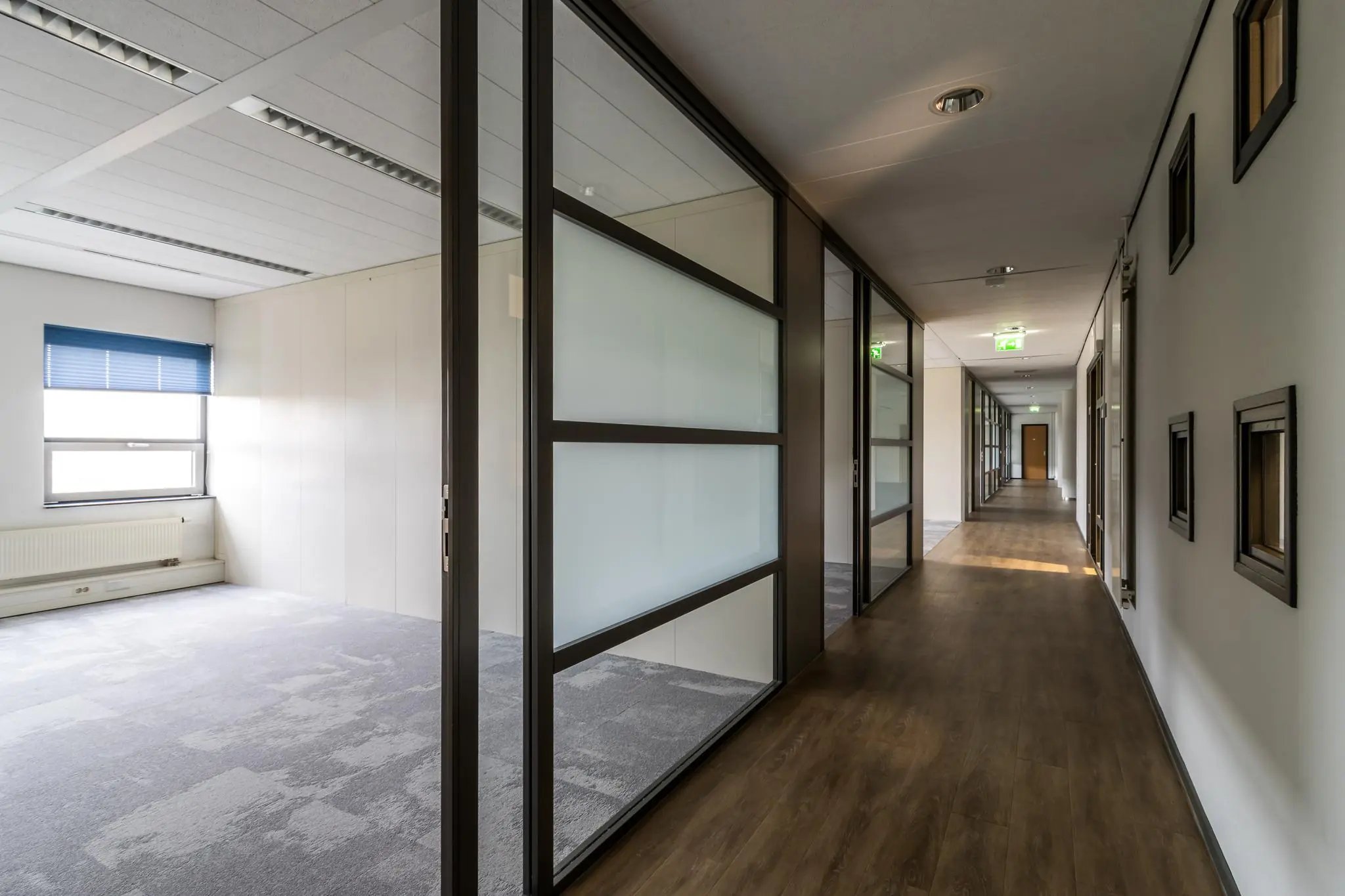 Lange gang met glazen kantoorwanden en houten vloer in een kantoorpand aan de Marconibaan.