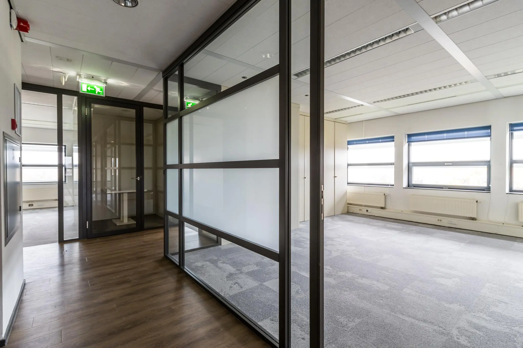 Modern kantoorpand aan de Marconibaan met glazen scheidingswanden en grote ramen met blauwe jaloezieën.