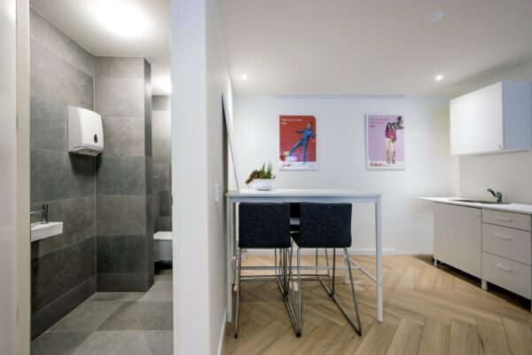 Moderne kantoorruimte met kleine keuken, zithoek en zicht op een betegeld toilet.