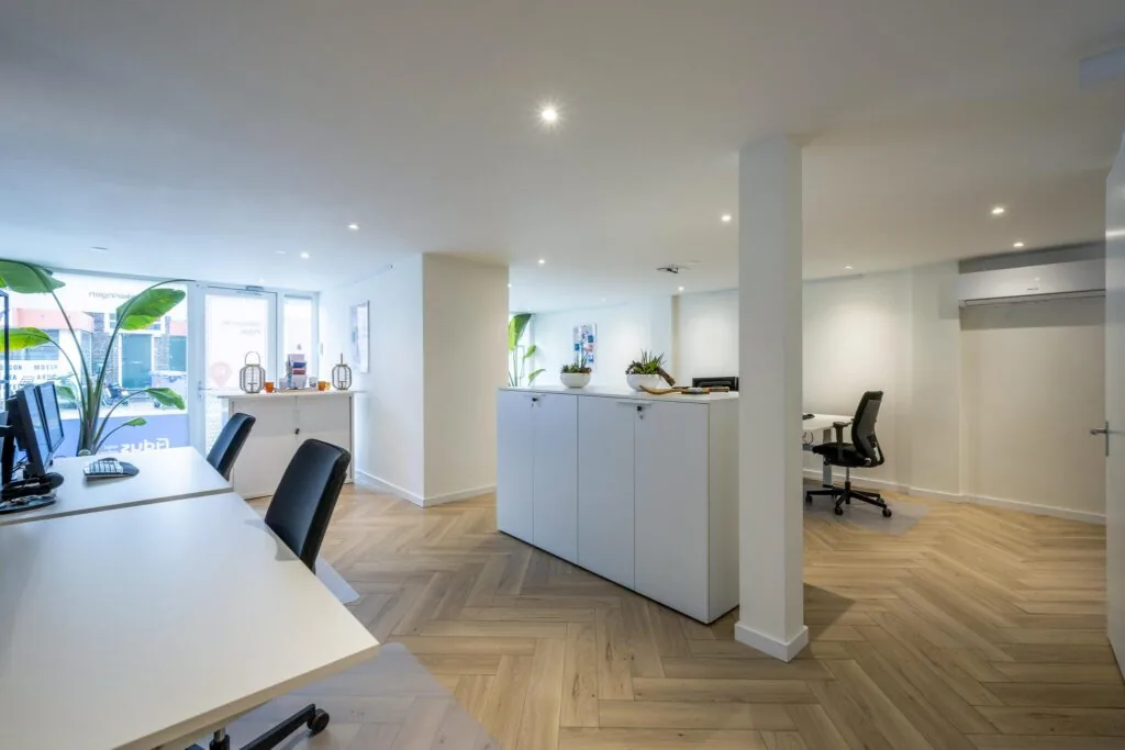 Modern en licht ingericht kantoor aan de Raadhuisstraat met werkplekken, planten en houten visgraatvloer.