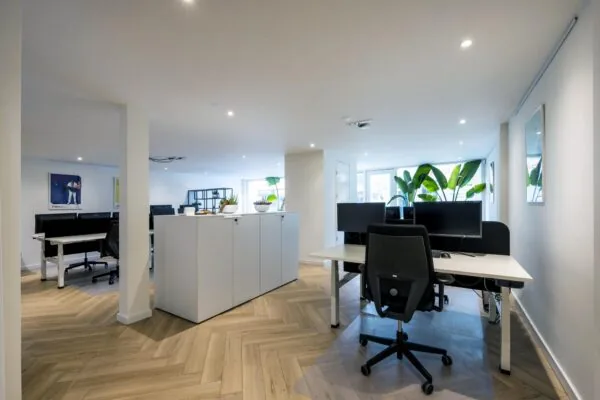 Modern kantoorinterieur aan de Raadhuisstraat met bureaus, planten en houten visgraatvloer.