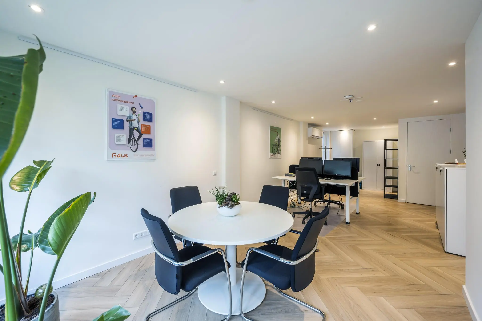 Moderne kantoorruimte aan de Raadhuisstraat met een ronde vergadertafel, werkplekken en een strakke, lichte inrichting.