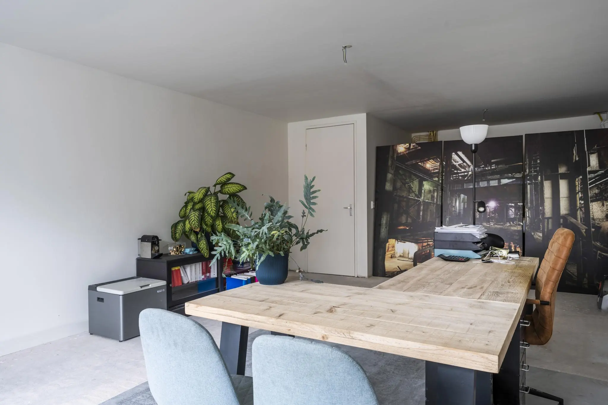 Moderne kantoorruimte aan de Raadhuisstraat met houten vergadertafel, planten en een kast met industriële fotoprint.