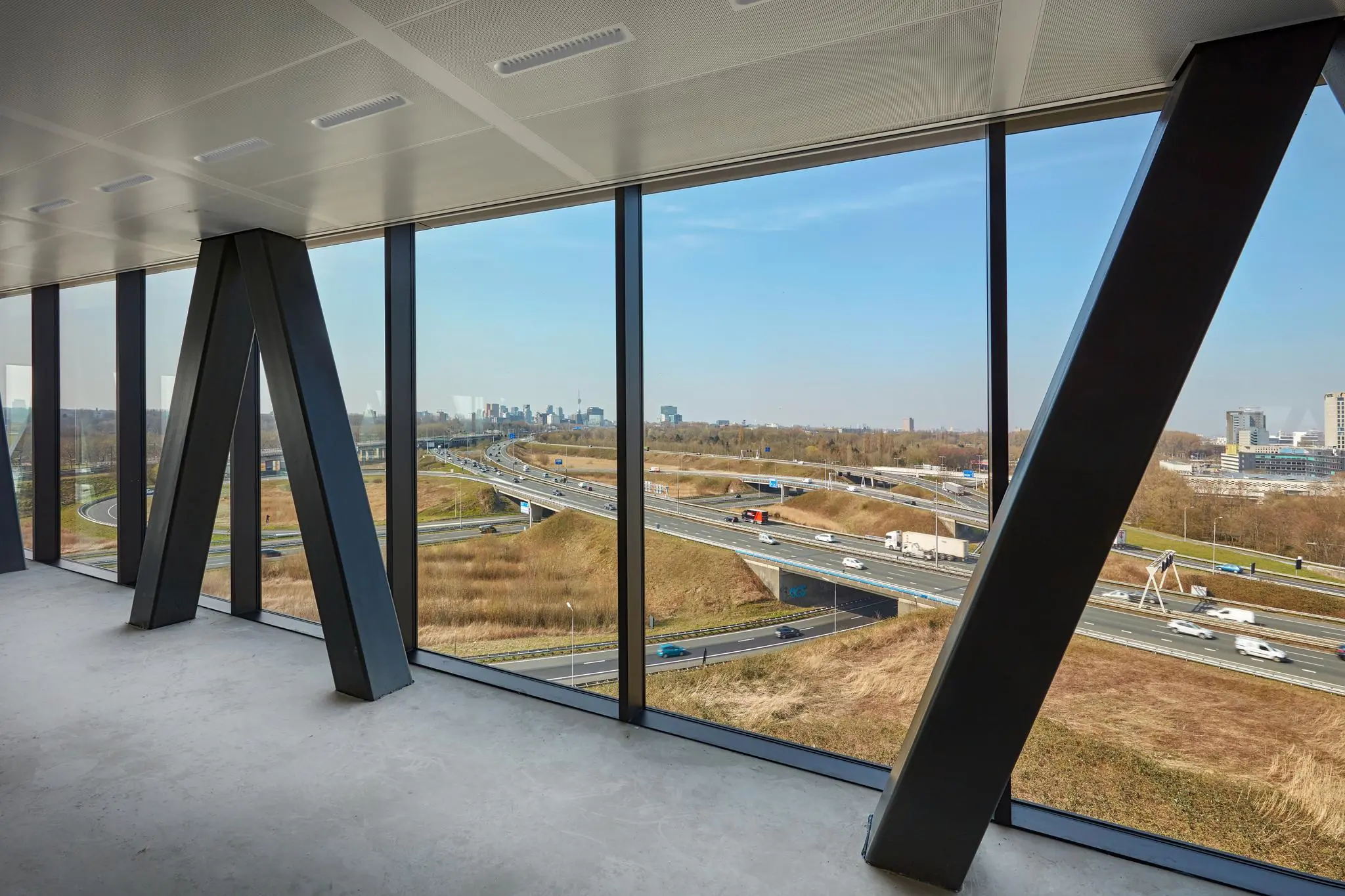 Uitzicht vanuit een modern kantoorgebouw aan de Joan Muyskenweg op een snelweg en de skyline van Amsterdam.
