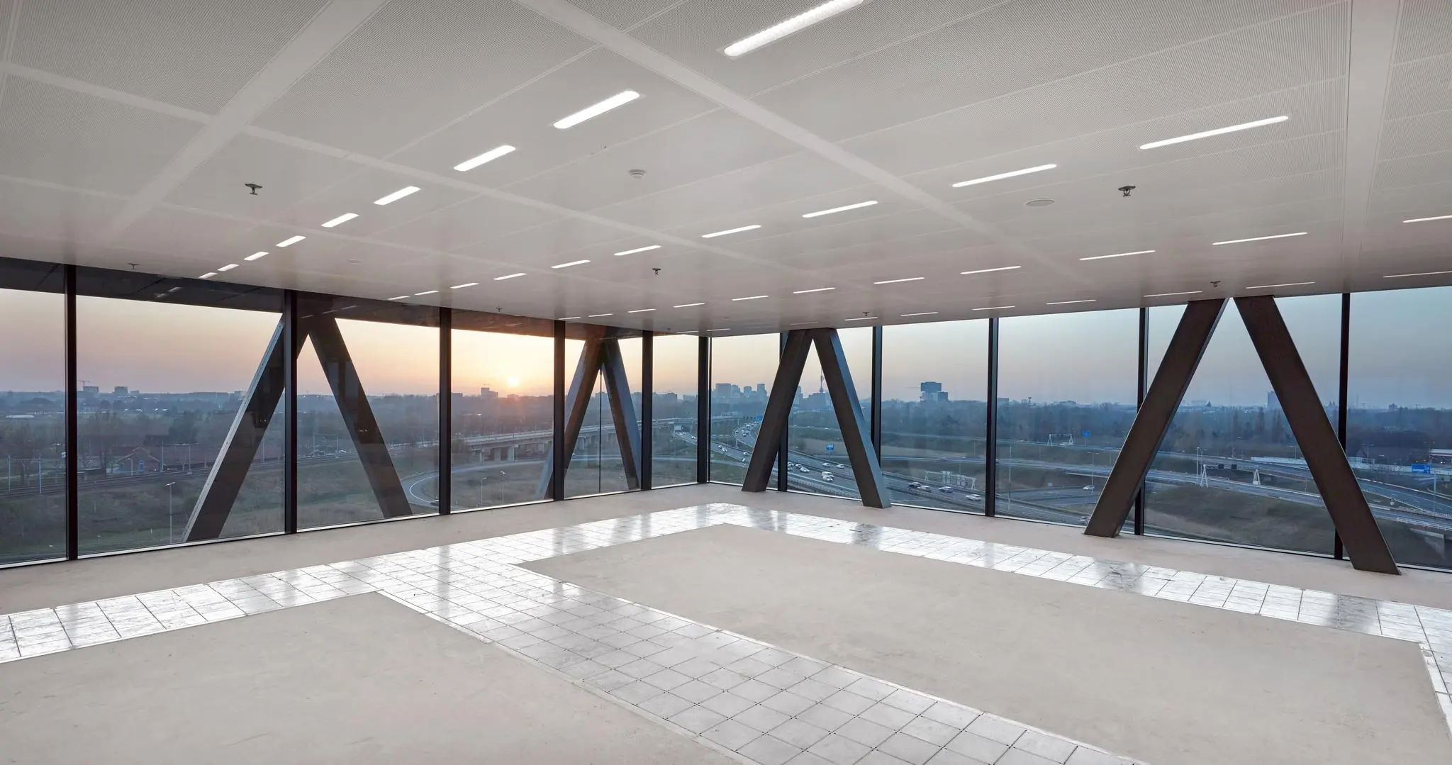 Leeg kantoorpand met grote ramen en uitzicht op de snelweg en stad bij zonsondergang aan de Joan Muyskenweg.