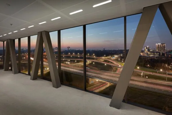 Uitzicht vanuit een modern kantoorgebouw aan de Joan Muyskenweg op een snelwegknooppunt bij zonsondergang.
