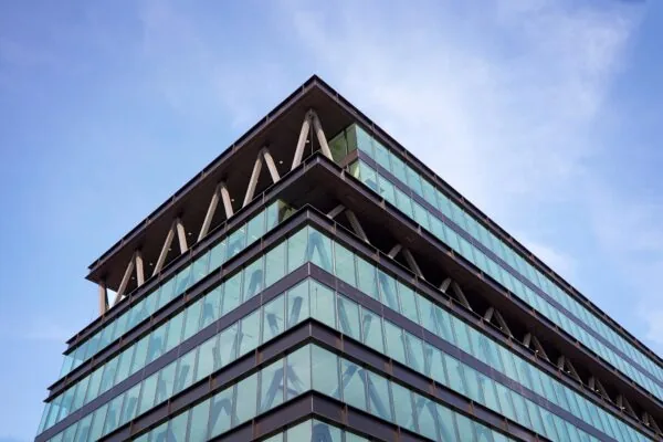 Modern kantoorgebouw met glazen gevel aan de Joan Muyskenweg, gefotografeerd vanaf een hoek onder een blauwe hemel.