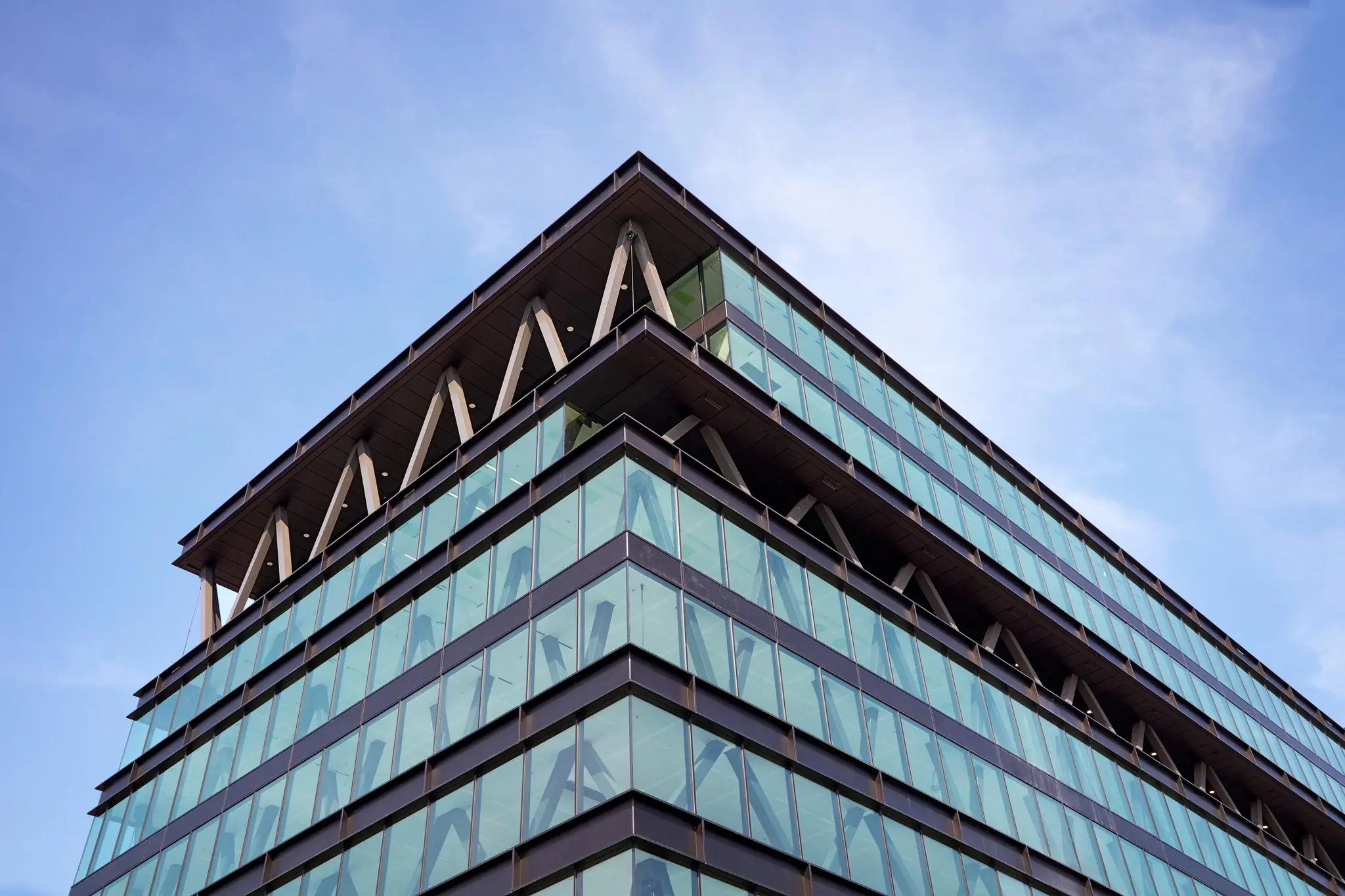 Modern kantoorgebouw met glazen gevel aan de Joan Muyskenweg, gefotografeerd vanaf een hoek onder een blauwe hemel.