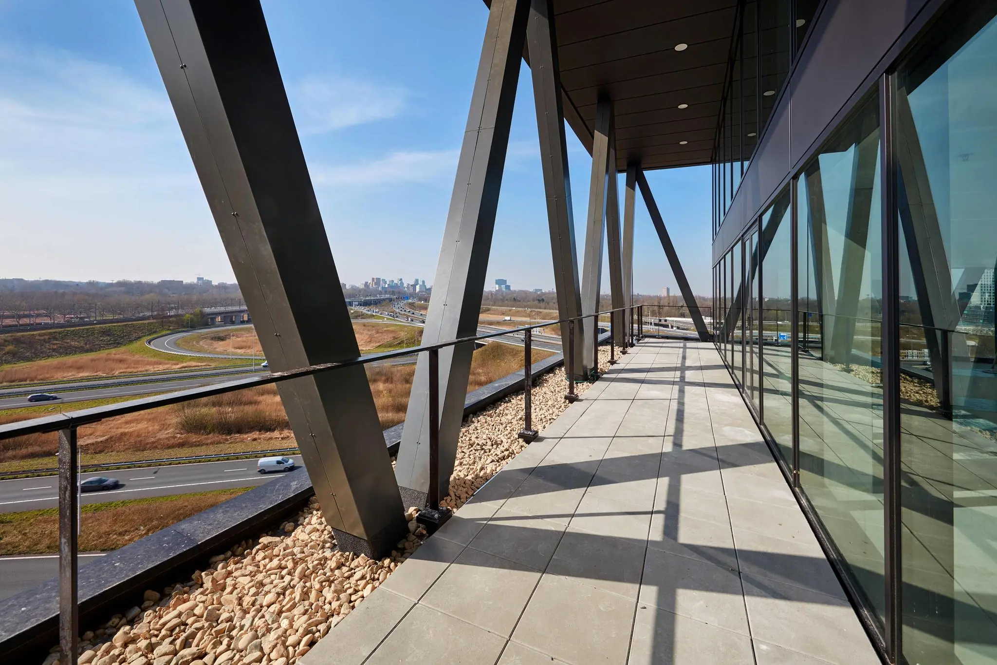 Moderne gevel met glazen wand en stalen constructie aan de Joan Muyskenweg, met uitzicht op snelwegen en de skyline van Amsterdam.